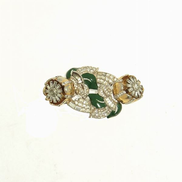 CORO -   MATERIAL: gold tone metal end enamel DESCRIPTION: a gold tone metal double clips, each designed as camelia flower with trembler centers enhanced by clear baguettes. Othes baguettes end pav&egrave; crystals enhanced the rest of the duette with dark green enamel leaves. The clips are marked Des. Pat. 110296 end USA Pat. Off. The forme is not marked. Patent number 110296, for the duette, was issued to Gene Verrecchio on June 26, 1938. There is a bit of wear on the gold tone in the high points. The booch is pubblished on "American Costume Jewelry" 1935-1950, Carla e Roberto Brunialti, ed. Mazzotta, 1997 MEASURES lenght 2,5 in.  