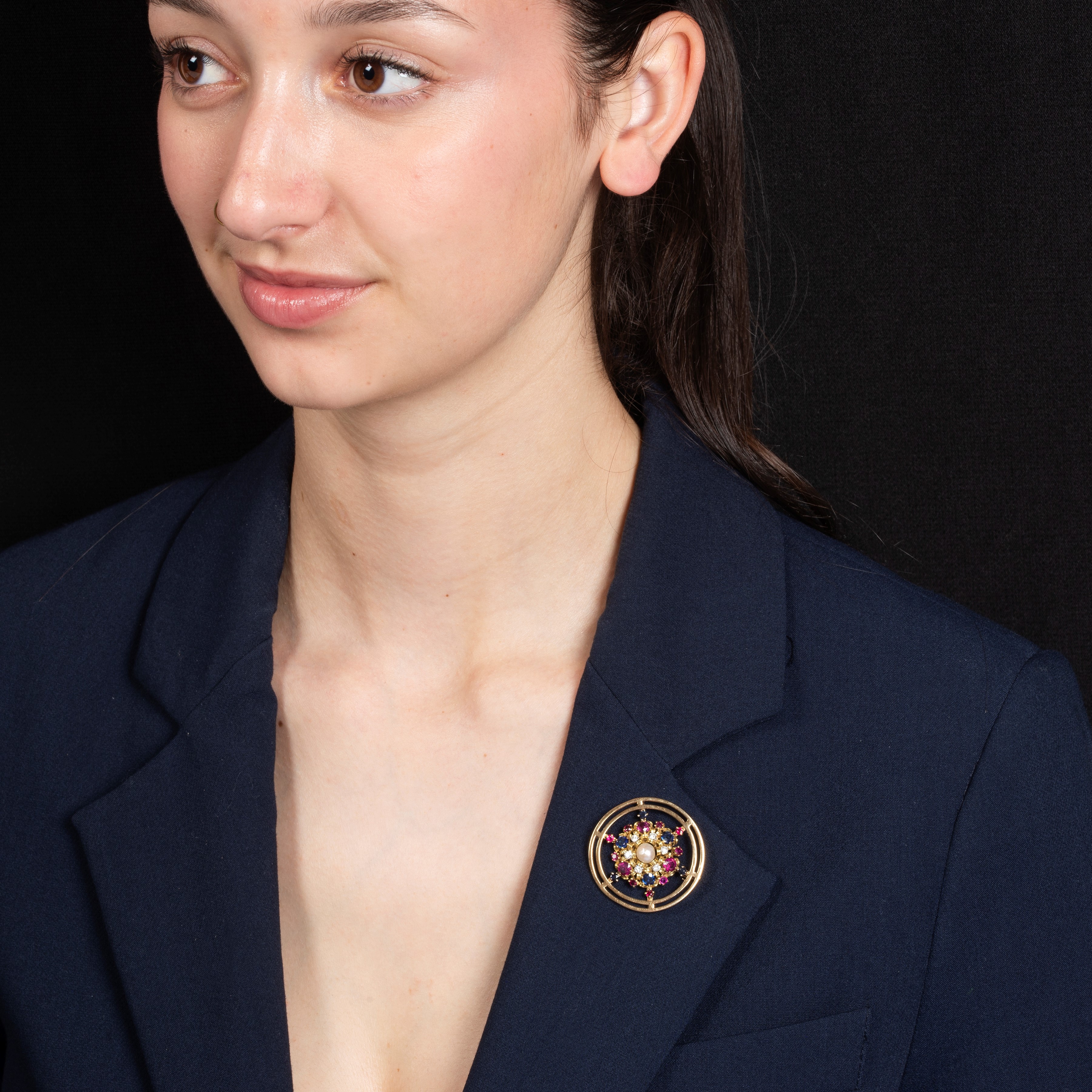 Spilla circolare in oro giallo 18 kt con diamanti, zaffiri, rubini e perla coltivata, anni Cinqua...